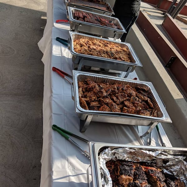 A buffet line of chafing dishes filled with various barbecued meats, including pulled pork and chicken.