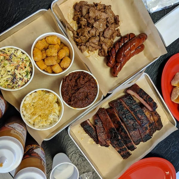 Overhead view of barbecue spread with ribs, sausage, brisket, coleslaw, mac and cheese, and tater tots.