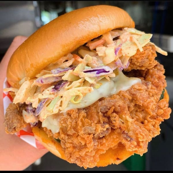 Crispy fried chicken sandwich with creamy coleslaw and white sauce on a brioche bun.