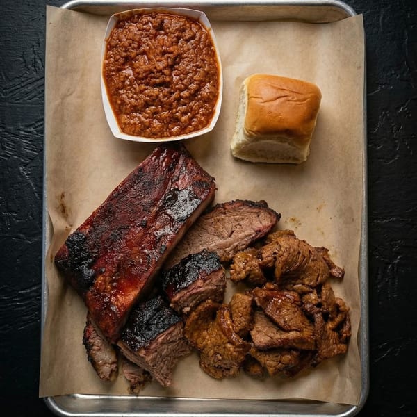 Barbecue platter with ribs, brisket, baked beans, and a dinner roll on a metal tray.