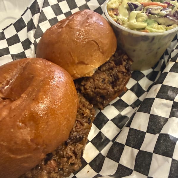 Two pulled pork sandwiches on buns with a side of coleslaw in a checkered paper-lined basket.